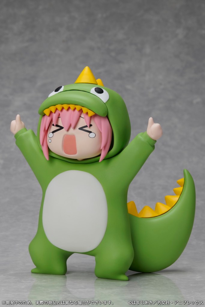 A cute figure of a character wearing a green dinosaur costume, featuring pink hair and an excited expression, standing with arms raised.