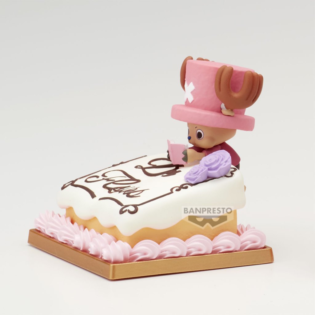 A collectible figure of Tony Tony Chopper from One Piece sitting on a cake, reading a book with a pink hat and decorated with roses.